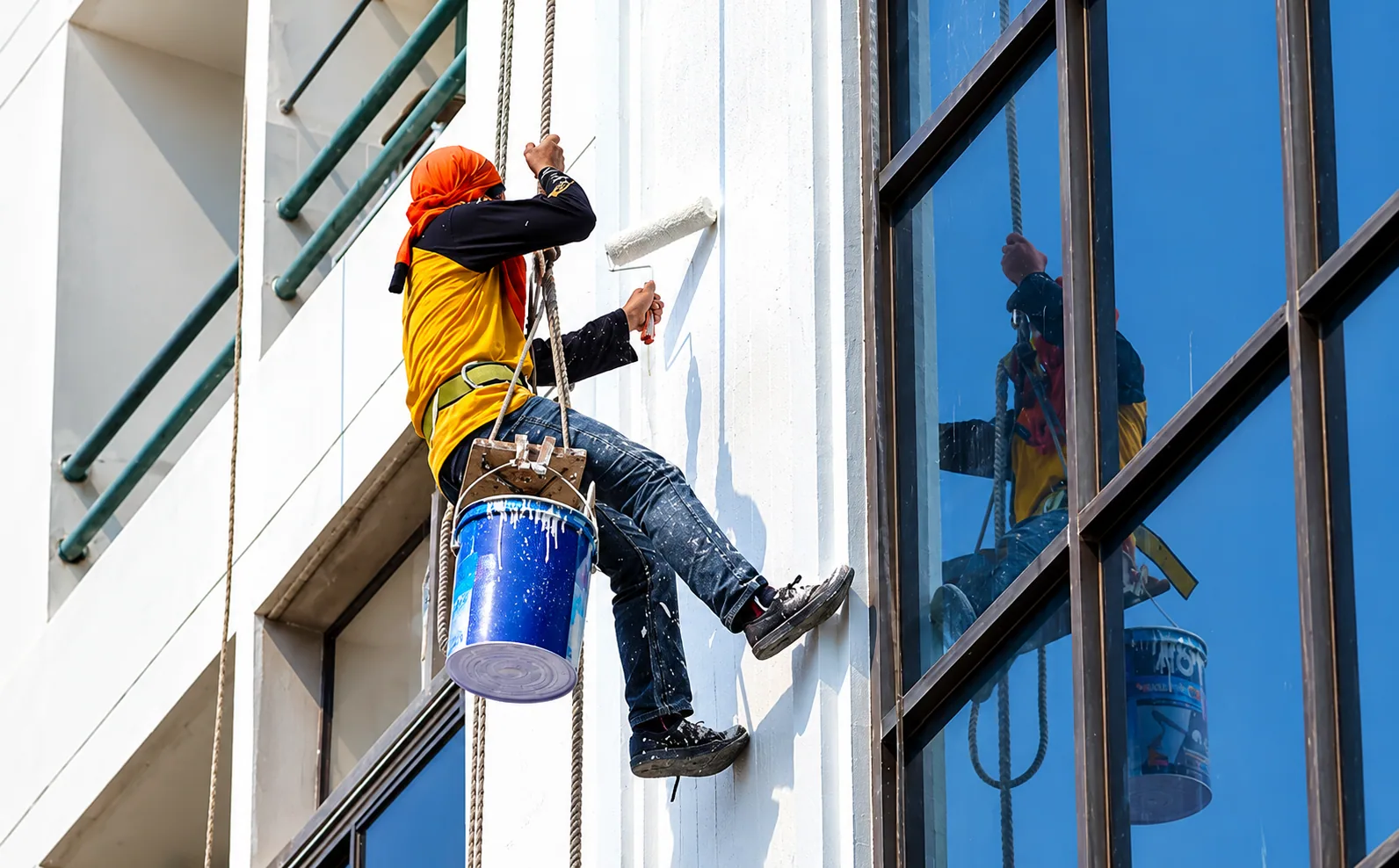 Profissional aplicando acabamento em fachada com acesso por corda